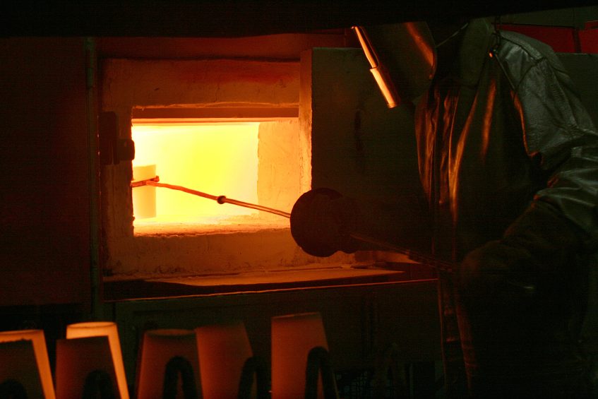 Glass blower shaping molten glass in dark workshop